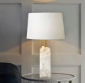 Biała lampa stołowa z tkaninowym kloszem i złotymi detalami.